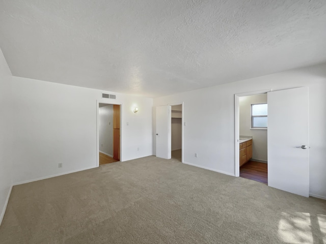 unfurnished bedroom with carpet floors, visible vents, a textured ceiling, and ensuite bath