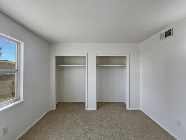 unfurnished bedroom featuring baseboards, visible vents, a textured ceiling, carpet flooring, and two closets