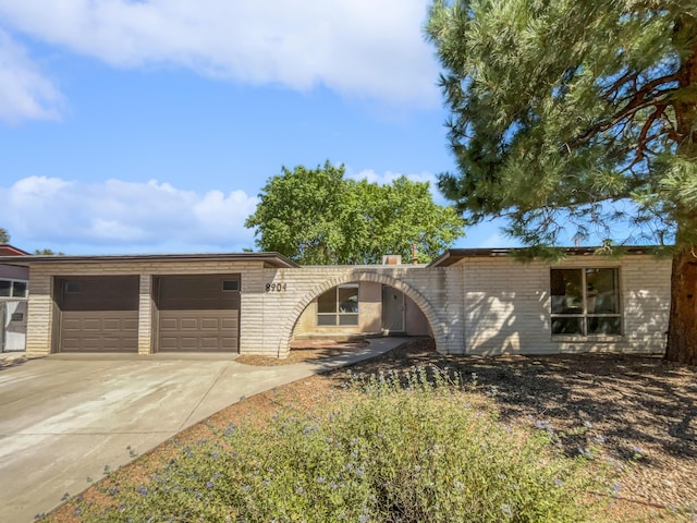 ranch-style house featuring concrete driveway, brick siding, and an attached garage