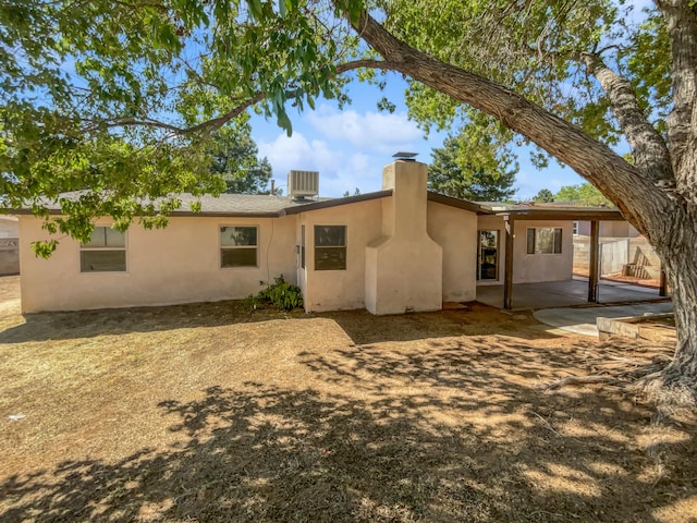 rear view of house featuring a patio, a chimney, cooling unit, and stucco siding