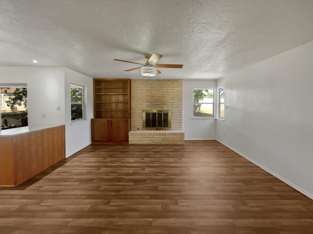 unfurnished living room with a textured ceiling, built in shelves, a brick fireplace, and wood finished floors