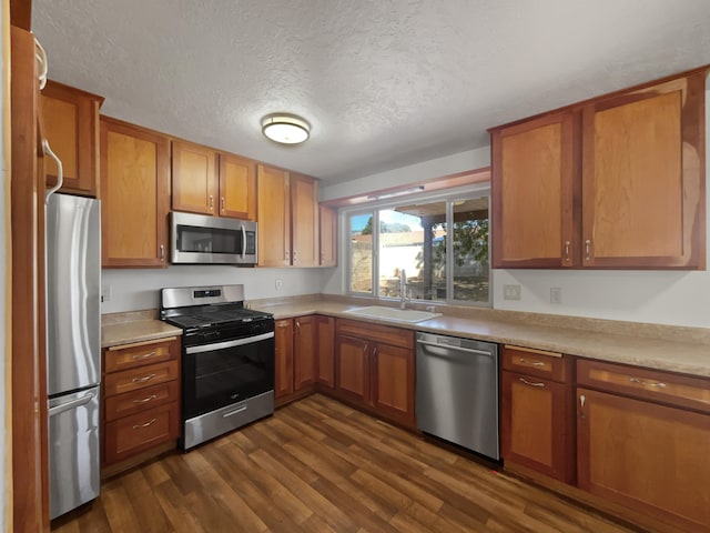 kitchen with appliances with stainless steel finishes, sink, a textured ceiling, and dark hardwood / wood-style flooring