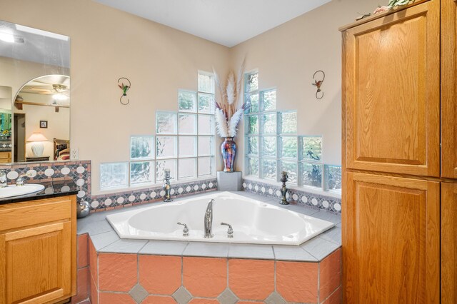 bathroom with a wealth of natural light, ceiling fan, tiled bath, and vanity