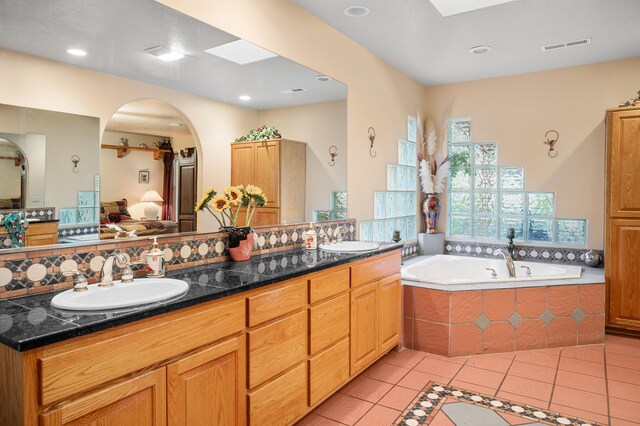 bathroom with tiled tub, backsplash, dual vanity, a skylight, and tile patterned floors