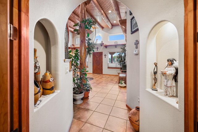 hall with light tile patterned floors, vaulted ceiling with beams, and wood ceiling