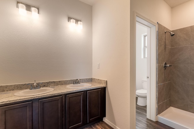 bathroom featuring tiled shower, hardwood / wood-style flooring, vanity, and toilet