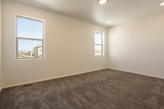 spare room with dark carpet and a textured ceiling