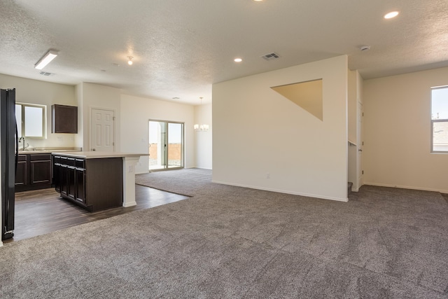 kitchen featuring dark brown cabinetry, sink, a center island, dark colored carpet, and a textured ceiling