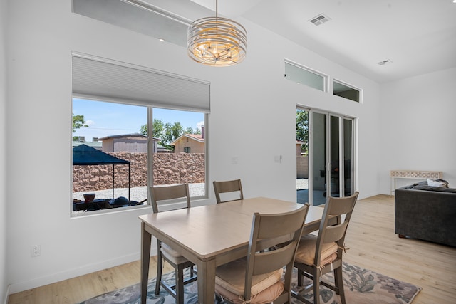 dining space with light wood finished floors, baseboards, visible vents, and a notable chandelier