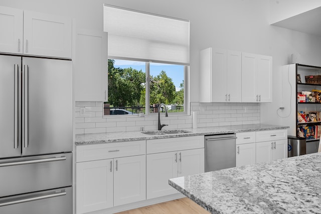 kitchen with stainless steel appliances, tasteful backsplash, white cabinetry, a sink, and light stone countertops