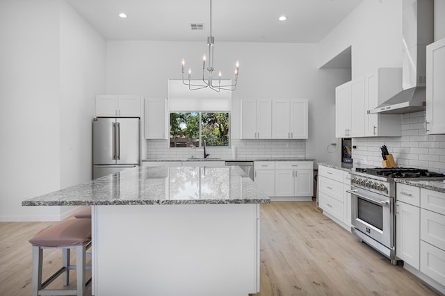 kitchen with premium appliances, wall chimney exhaust hood, a kitchen island, light stone counters, and white cabinetry