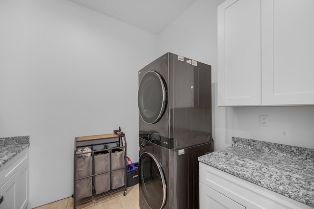 laundry area with cabinet space, light wood-style flooring, and stacked washer / dryer