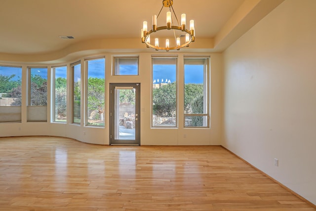 empty room with visible vents, light wood-style flooring, and an inviting chandelier