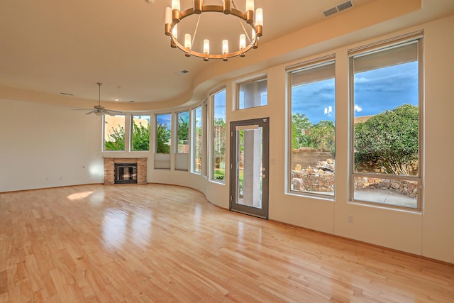 unfurnished living room with a glass covered fireplace, ceiling fan with notable chandelier, visible vents, and light wood finished floors