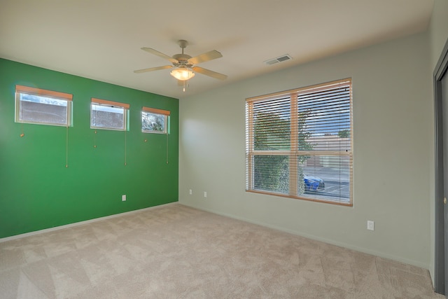 carpeted spare room with baseboards, visible vents, and ceiling fan