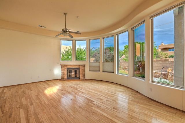 unfurnished sunroom with a stone fireplace, visible vents, a wealth of natural light, and ceiling fan