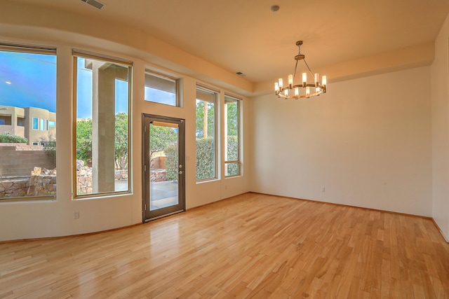 empty room with an inviting chandelier, light wood-style floors, and visible vents