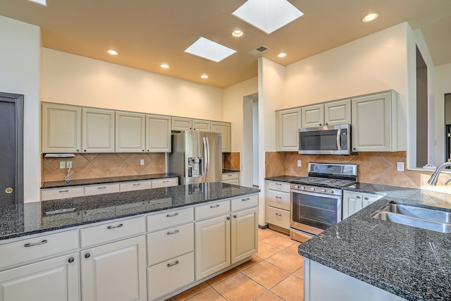 kitchen with a skylight, stainless steel appliances, sink, white cabinets, and light tile patterned flooring