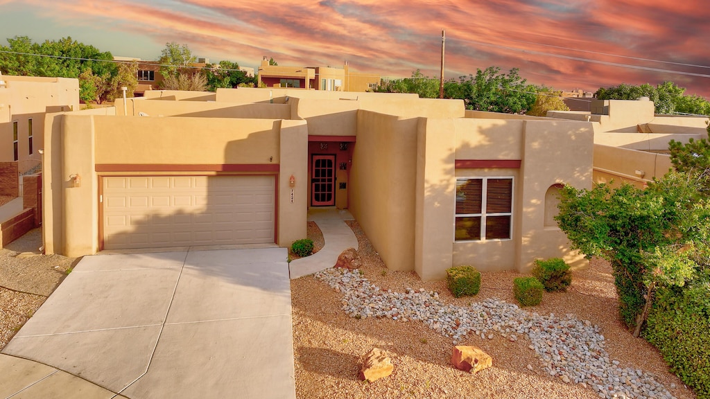 adobe home with concrete driveway, an attached garage, and stucco siding