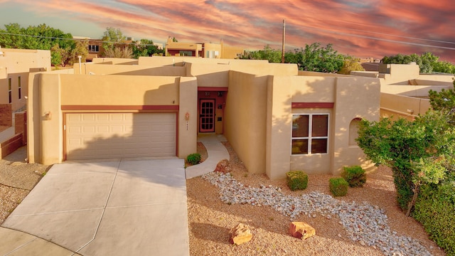 adobe home with concrete driveway, an attached garage, and stucco siding