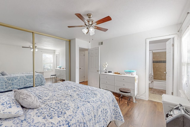 bedroom with light wood-type flooring, connected bathroom, ceiling fan, and a closet