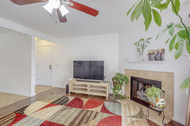 living room with wood-type flooring, ceiling fan, and a tile fireplace