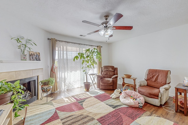 living room with light wood-type flooring, a textured ceiling, ceiling fan, and a tile fireplace