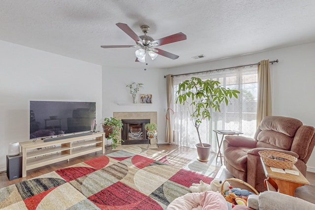 living room with ceiling fan, hardwood / wood-style flooring, a tiled fireplace, and a textured ceiling