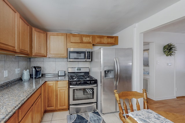 kitchen featuring appliances with stainless steel finishes, light hardwood / wood-style flooring, dark stone counters, and backsplash