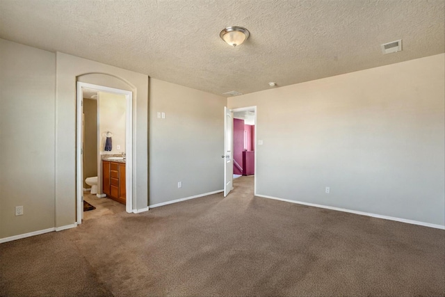 unfurnished bedroom with carpet flooring, a textured ceiling, and ensuite bath