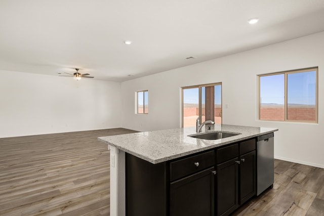 kitchen with light stone counters, a kitchen island with sink, a sink, stainless steel dishwasher, and light wood finished floors