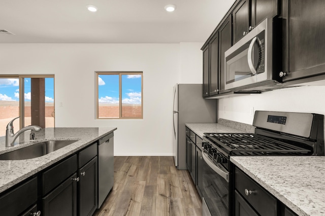 kitchen with visible vents, appliances with stainless steel finishes, light stone counters, wood finished floors, and a sink