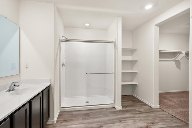 full bathroom with a walk in closet, a stall shower, vanity, wood finished floors, and baseboards