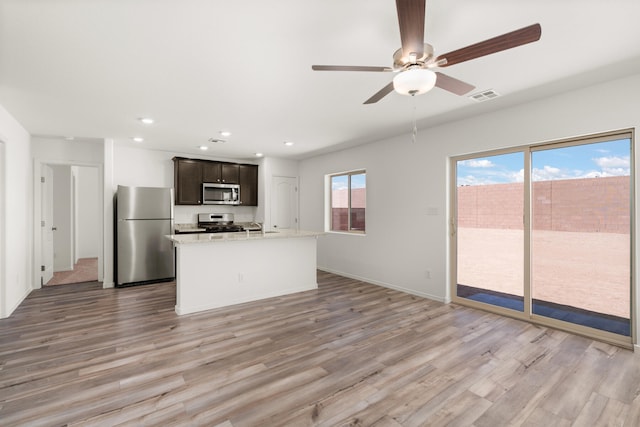 kitchen with light hardwood / wood-style flooring, light stone countertops, stainless steel appliances, ceiling fan, and a kitchen island with sink