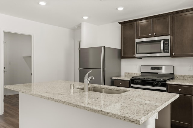 kitchen with an island with sink, light stone counters, dark hardwood / wood-style floors, and appliances with stainless steel finishes