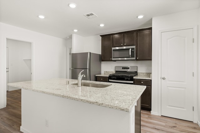 kitchen with a center island with sink, stainless steel appliances, sink, and light hardwood / wood-style floors