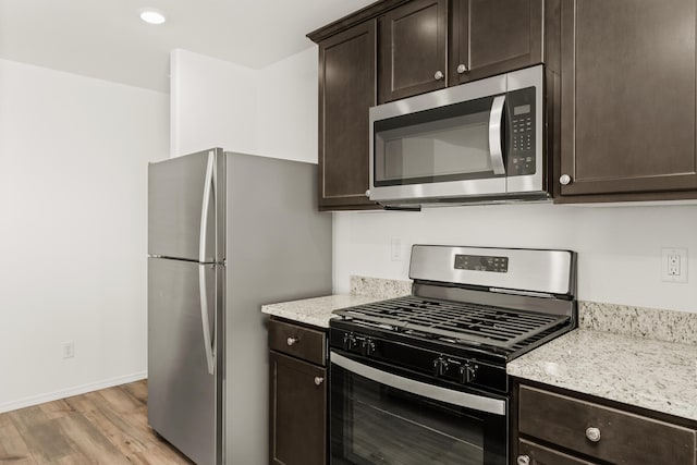 kitchen featuring dark brown cabinets, light hardwood / wood-style flooring, stainless steel appliances, and light stone countertops