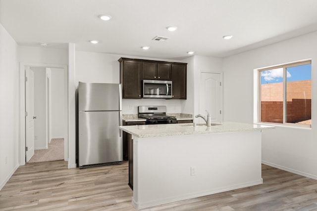 kitchen featuring light wood-type flooring, stainless steel appliances, sink, dark brown cabinets, and an island with sink