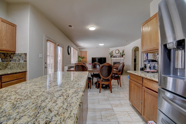 kitchen featuring stainless steel refrigerator with ice dispenser, decorative backsplash, and light stone countertops