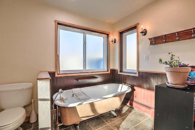 bathroom with wainscoting, toilet, a baseboard radiator, wood walls, and a freestanding tub