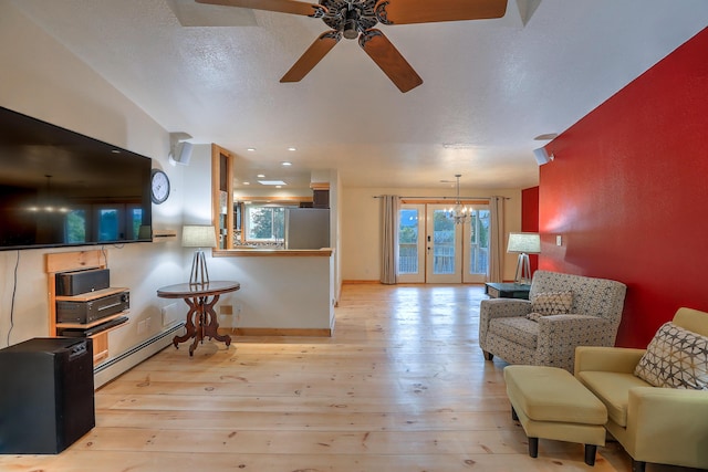 living area with ceiling fan with notable chandelier, baseboard heating, hardwood / wood-style flooring, and baseboards