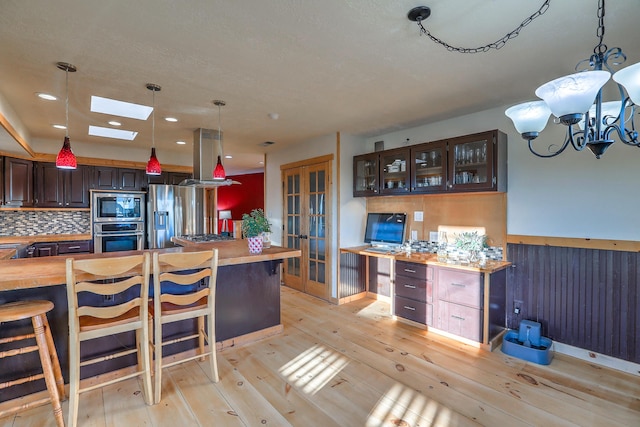 kitchen with light wood-type flooring, butcher block countertops, appliances with stainless steel finishes, and glass insert cabinets