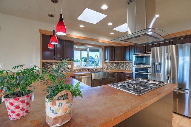 kitchen featuring a skylight, island exhaust hood, backsplash, appliances with stainless steel finishes, and a peninsula