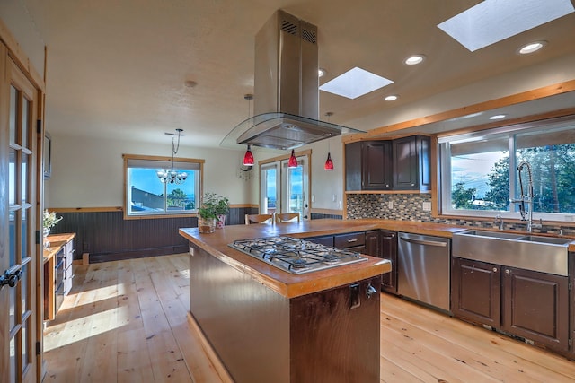 kitchen featuring a sink, light wood-style floors, appliances with stainless steel finishes, wainscoting, and island exhaust hood