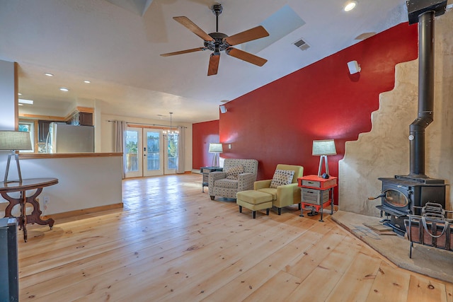 living area with a wood stove, a ceiling fan, visible vents, and hardwood / wood-style floors