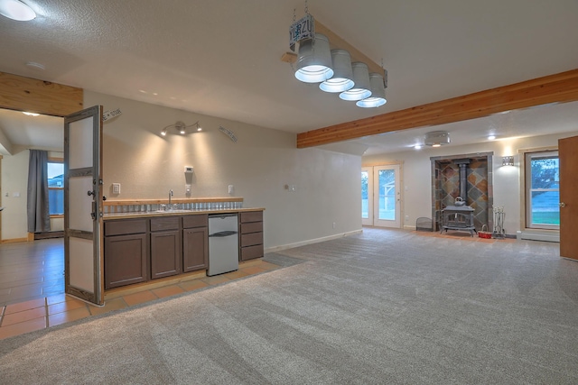 kitchen with light colored carpet, beamed ceiling, a wood stove, a sink, and a wealth of natural light