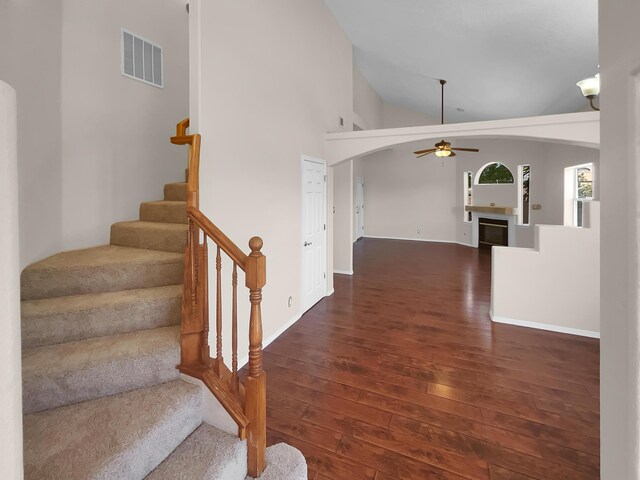 staircase with ceiling fan, hardwood / wood-style floors, and high vaulted ceiling