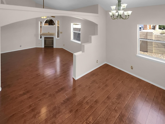 interior space with ceiling fan with notable chandelier, dark wood-type flooring, a glass covered fireplace, and baseboards