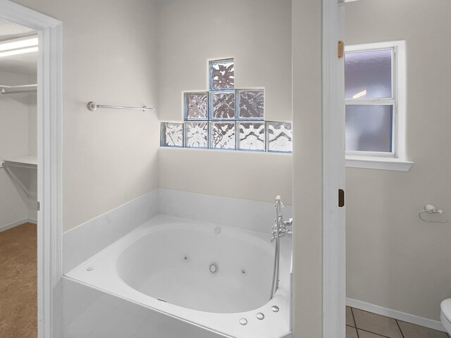 bathroom with a tub to relax in, toilet, and tile patterned flooring