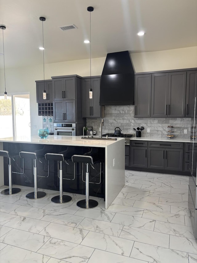 kitchen with oven, marble finish floor, custom range hood, a kitchen breakfast bar, and decorative backsplash